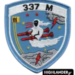 Cyan embroidered patch with ghost riding red missiles, stars, clouds, yellow squadron emblem, "337 M" text, and blue border.