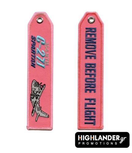 Ροζ κεντητό μπρελόκ αεροπορίας C-27J Spartan. Η μία πλευρά δείχνει το αεροσκάφος και κείμενο 354 ΜΤΜ. Η άλλη γράφει "REMOVE BEFORE FLIGHT" με μπλε γράμματα.