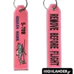 Pink embroidered aviation keychain for S-70B Aegean Hawk. Side A shows the helicopter and unit text. Side B shows "REMOVE BEFORE FLIGHT" in black text.