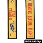 Double-sided embroidered flight tag keychain in yellow. Side 1: Vertical red text "T-6A TEXAN II" with a detailed embroidery of the blue and white trainer aircraft. Side 2: Vertical red text "REMOVE BEFORE FLIGHT".