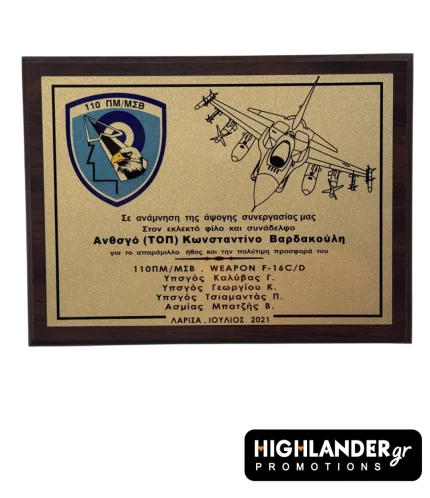 Ξύλινη στρατιωτική πλακέτα της 110 ΠΜ. Αριστερά το έμβλημα της Μονάδας, δεξιά σχέδιο F-16 και στο κέντρο κείμενο αφιέρωσης σε χρυσή μεταλλική επιφάνεια.