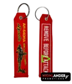 Red embroidered keychain showing AH-64DHA Apache helicopter on one side and Remove Before Attack text in white on the other side.