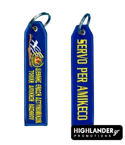 Blue embroidered keychain for IPA Lasithi. Side A shows the map of Crete, Greek flag, and Greek text. Side B shows the motto "SERVO PER AMIKECO" in yellow letters.