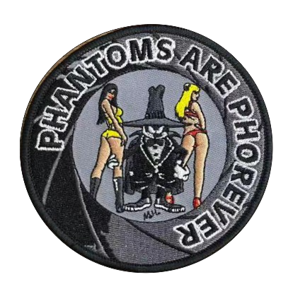 Στρογγυλό κεντητό σήμα με το κείμενο "PHANTOMS ARE PHOREVER". Στο κέντρο απεικονίζεται η μασκότ Spook του F-4 Phantom ανάμεσα σε δύο γυναίκες με μαγιό σε γκρι φόντο.