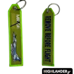 Olive green embroidered keychain from Highlander Promotions. Side A: Mirage 2000-5 aircraft and text. Side B: "REMOVE BEFORE FLIGHT" in dark blue lettering.