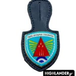 This dark blue leather badge hanger features a shield-shaped enamel badge with a vibrant light blue background, a prominent red arrowhead insignia, and radiating yellow stripes, all outlined in a metallic finish. Designed as an official holder for the 116 Combat Wing, it proudly displays the Greek motto "Para Dynamin Tolmitai," offering a distinguished utility for military personnel to showcase unit affiliation.