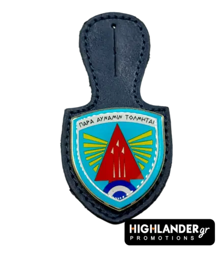 This dark blue leather badge hanger features a shield-shaped enamel badge with a vibrant light blue background, a prominent red arrowhead insignia, and radiating yellow stripes, all outlined in a metallic finish. Designed as an official holder for the 116 Combat Wing, it proudly displays the Greek motto "Para Dynamin Tolmitai," offering a distinguished utility for military personnel to showcase unit affiliation.