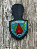 A navy blue leather badge holder featuring the 116 Combat Wing enamel crest with a red arrowhead, yellow wings, and the Greek motto "Para Dynamin Tolmitai".