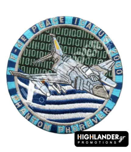 Round blue and silver embroidered military morale patch showing an F-4E Phantom jet over the Greek flag with a digital binary code background.